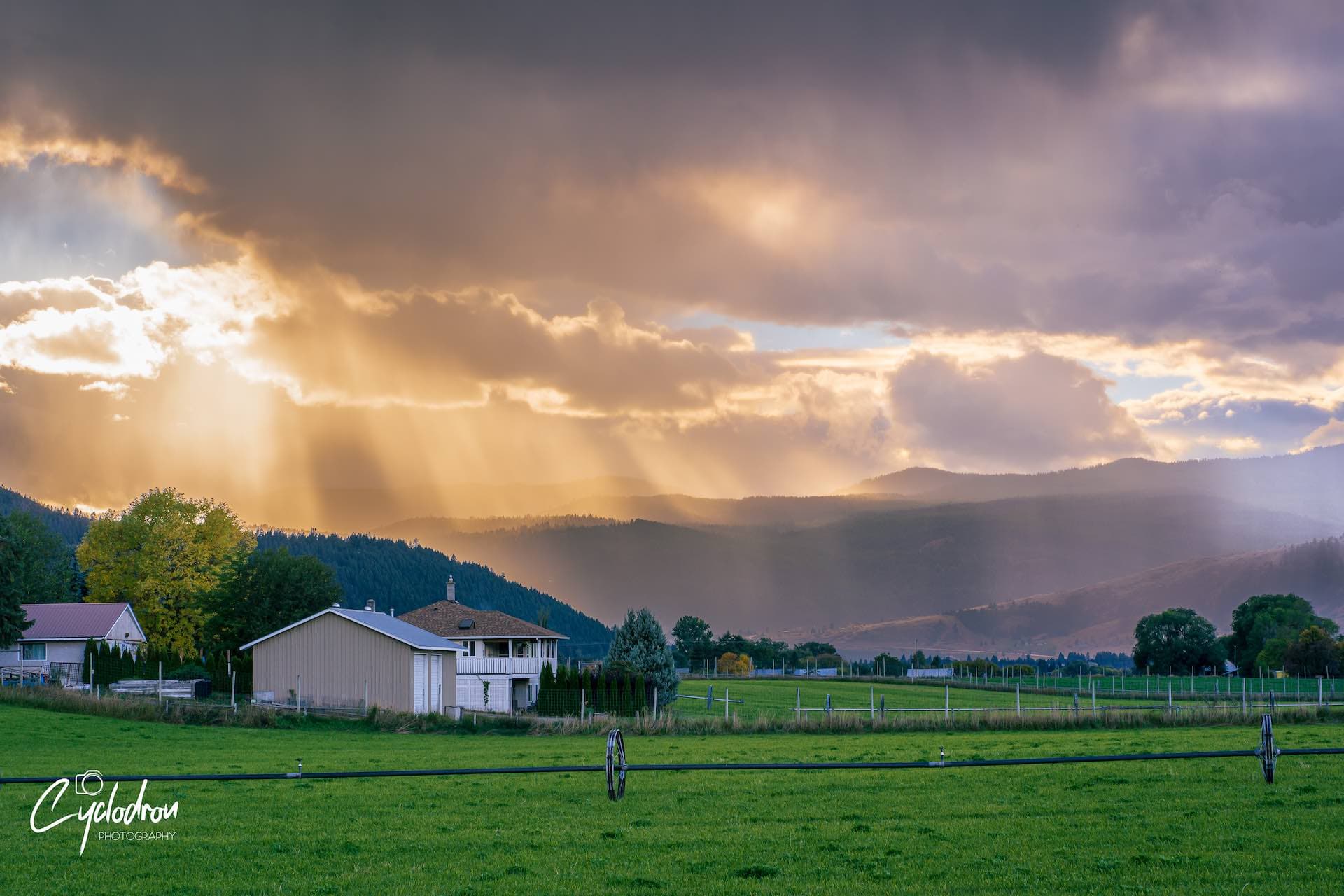 Dramatic god rays through storm clouds over rural farmland with mountain backdrop