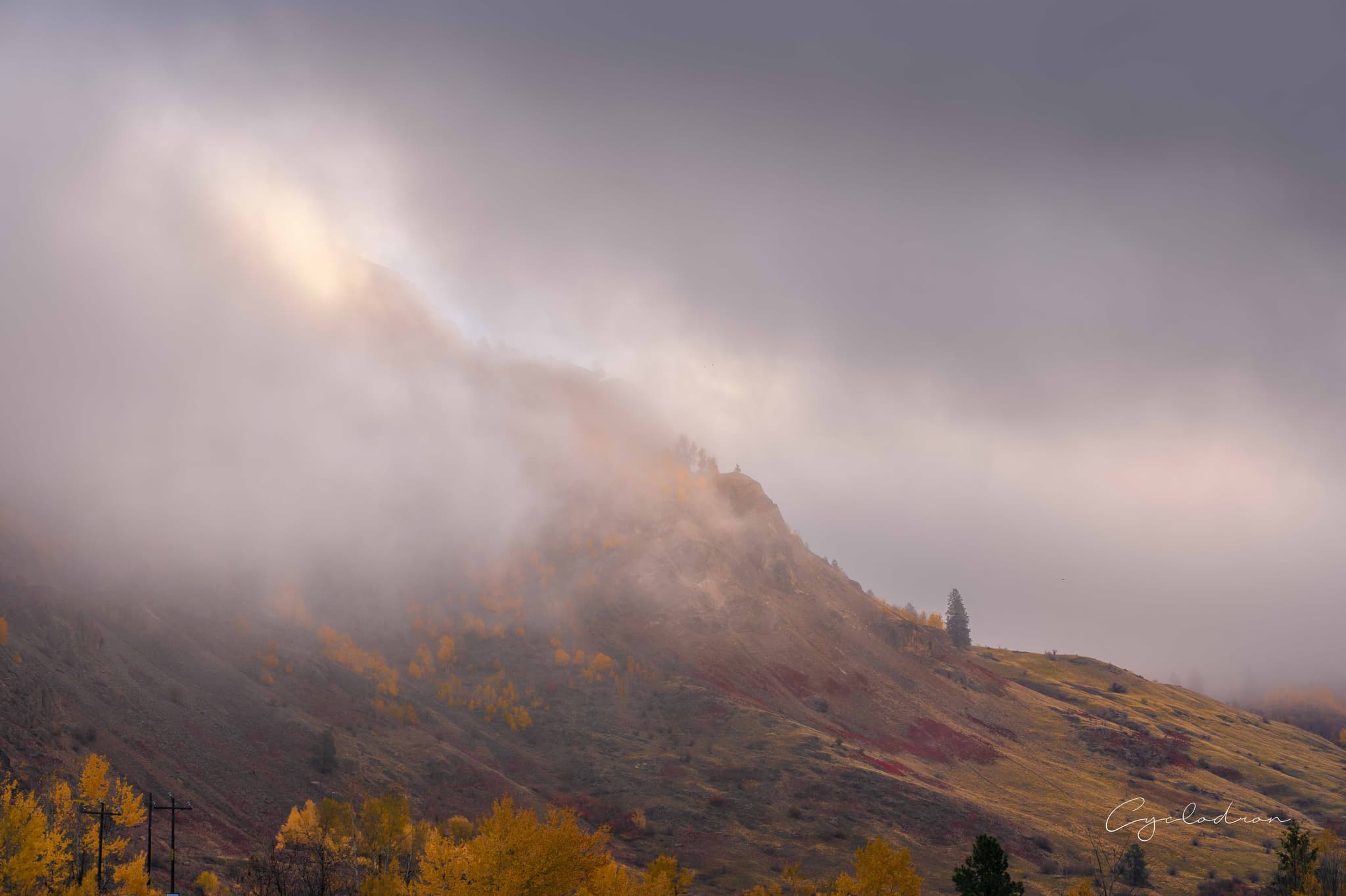 Misty mountain peak with autumn colors emerging through clouds