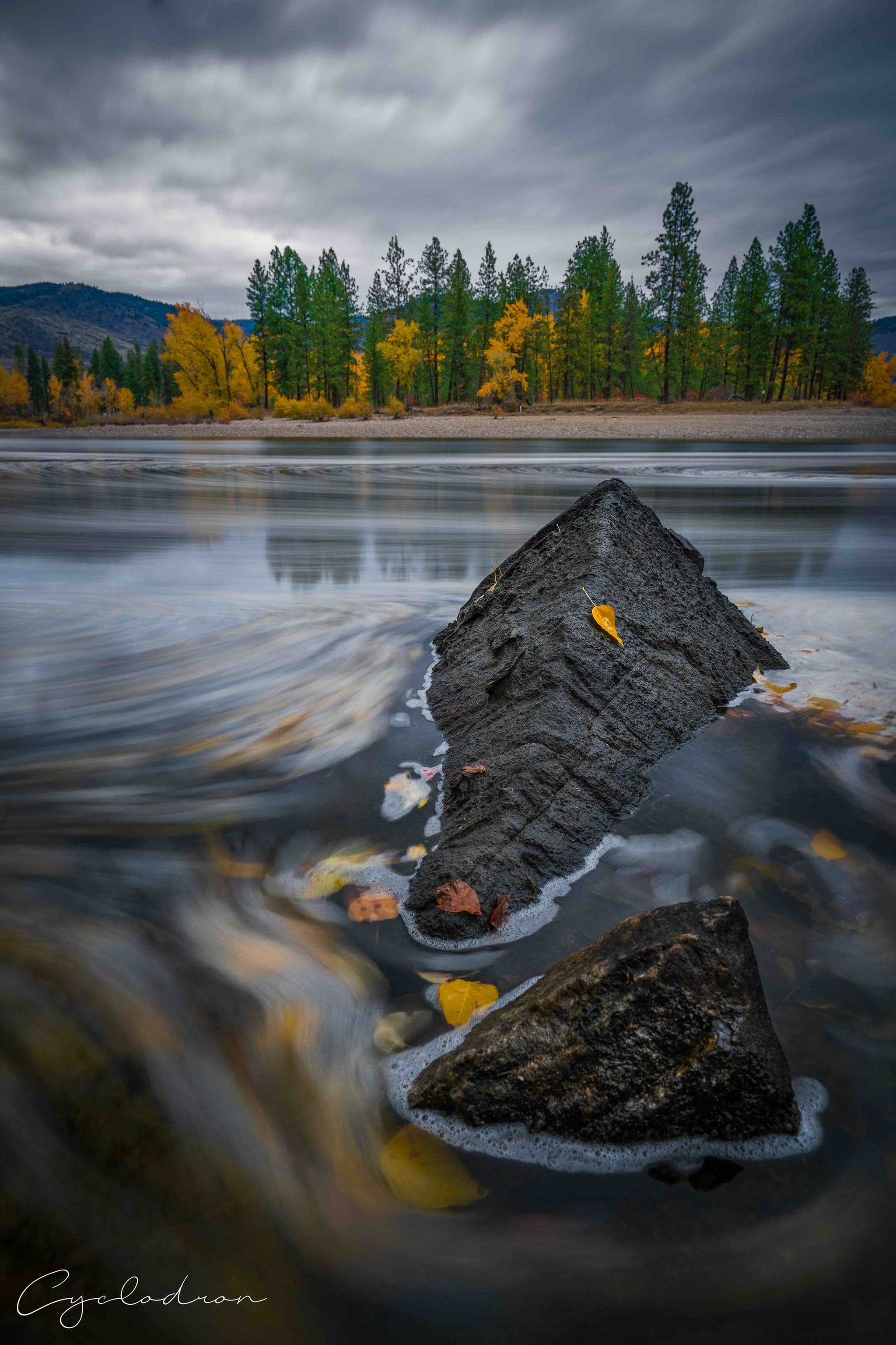 Long exposure of flowing water around rocks with autumn forest backdrop