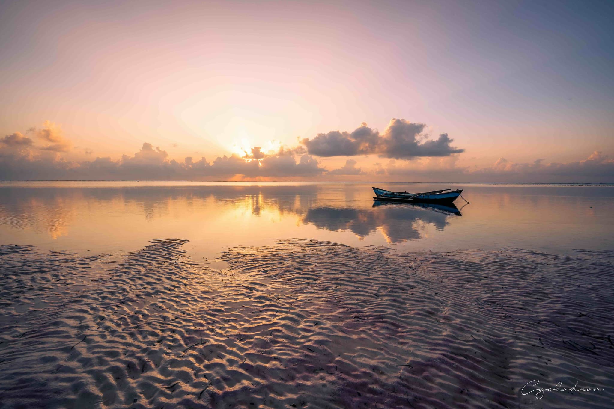 Serene sunrise with lone boat on calm water, golden reflections and gentle ripples