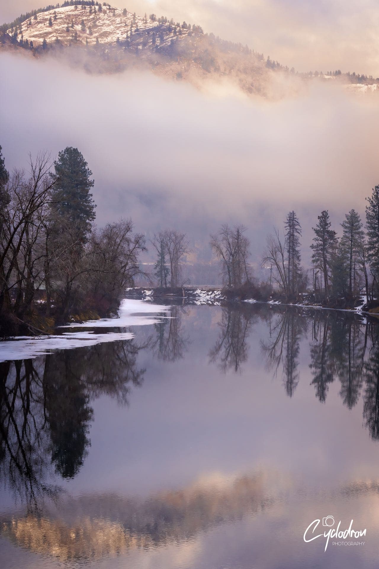 Misty winter river with fog rolling over snow-covered mountains