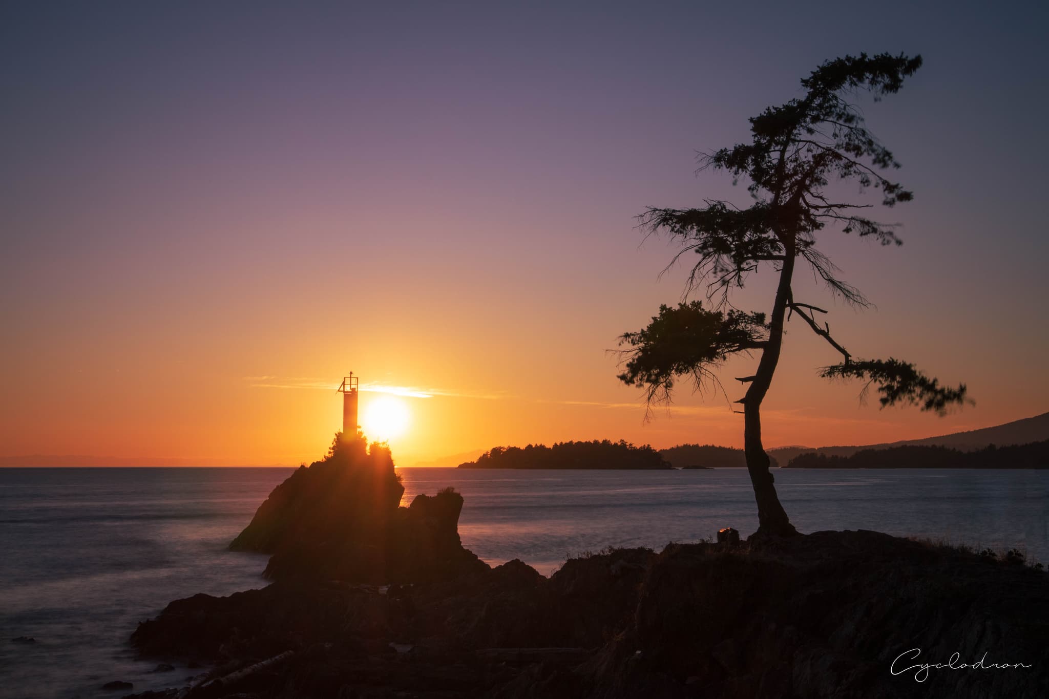 Coastal lighthouse silhouette at golden hour with windswept tree