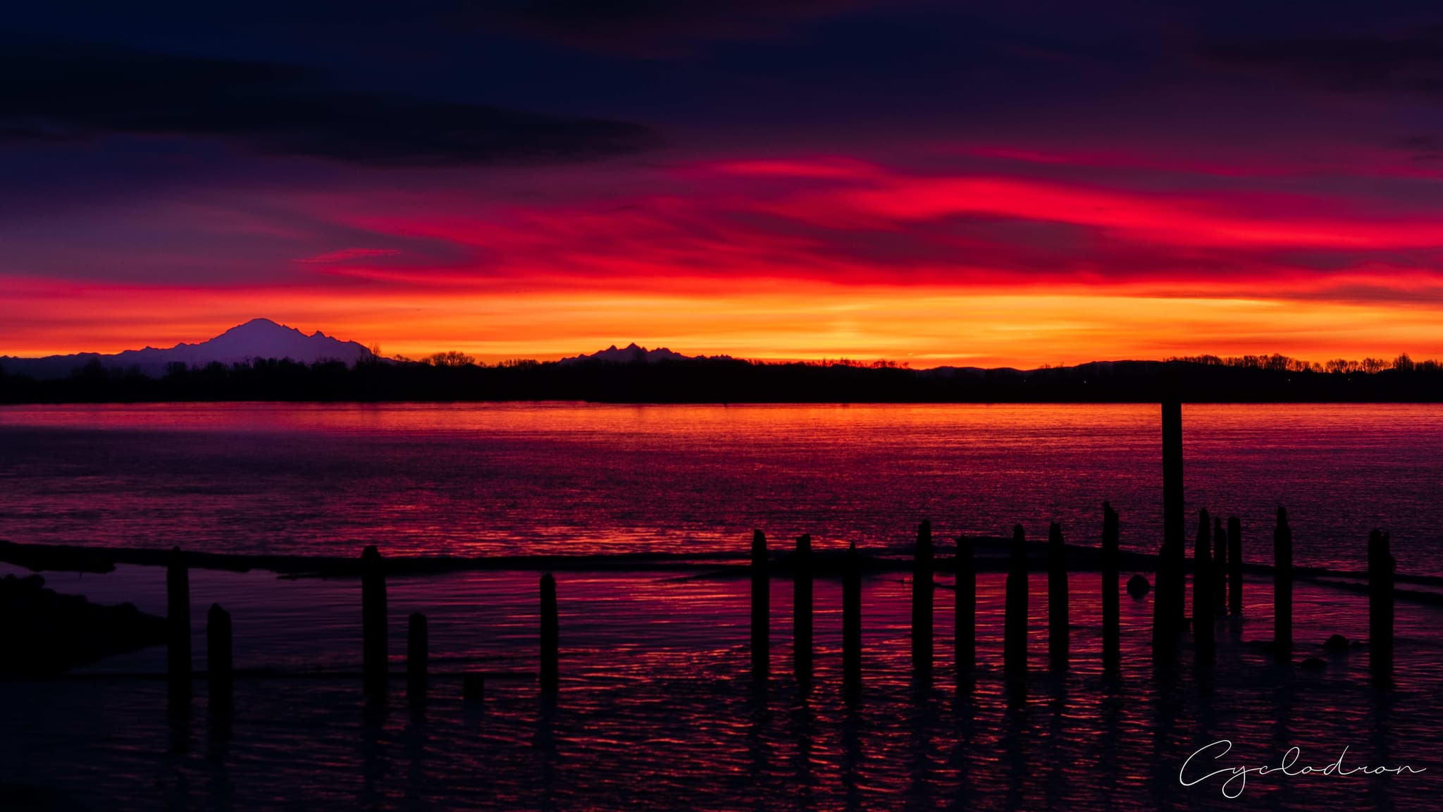 Dramatic red and orange sunset over mountain range with dock pilings